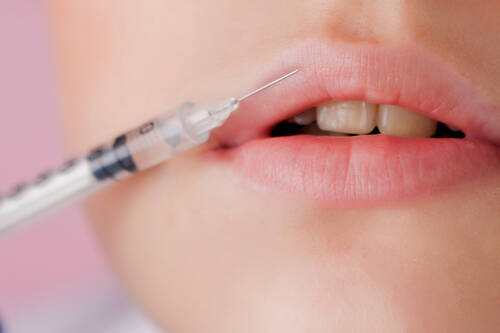 Doctor gloves giving woman botox injections lips pink background